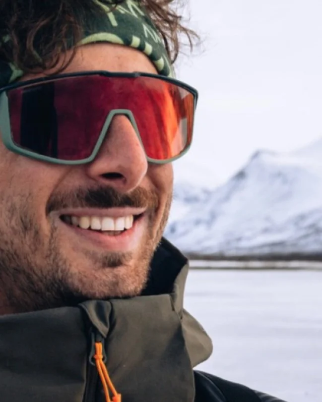 Portrait de Hugues Madier en montagne, bandeau et lunettes de soleil, sommets enneigés derrière lui