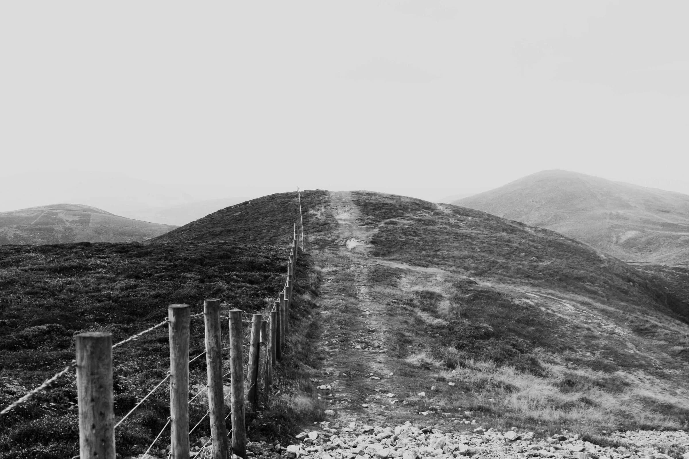 Clôture et sentier sur une colline, en noir et blanc